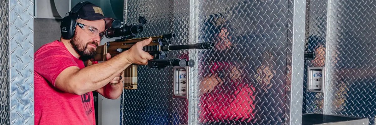 Atış poligonunda hedef tahtasına nişan alan bir kişi ve yanında tabanca aksesuarları